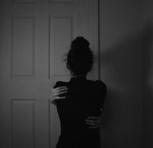 black and white emotive image of women embracing her self, captured from the back with heavy shadows